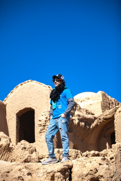 During the day, dressed in a blue jacket and grey trousers man standing on the brown rock formation
